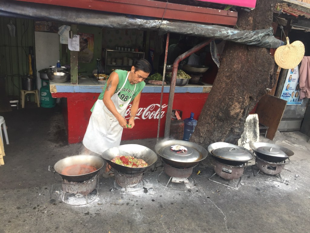 The cook tending a row of kawali over charcoal at Sosing's Carinderia