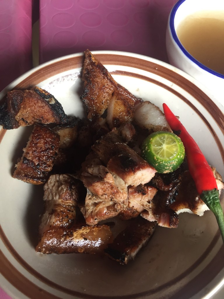 A plate of grilled inihaw na liempo with calamansi and chili